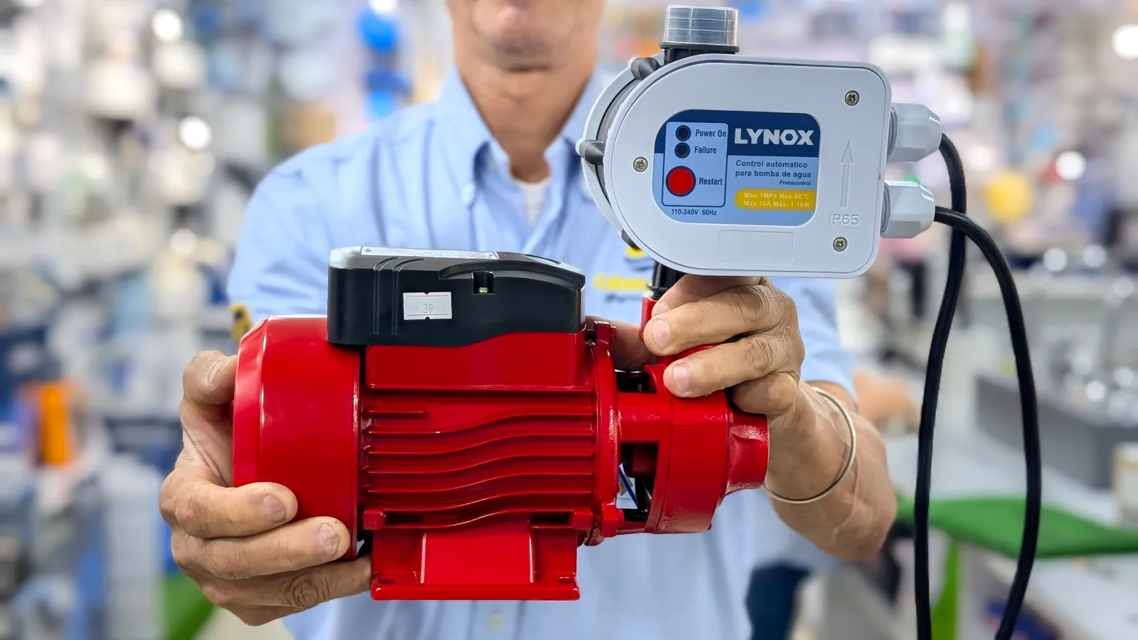 Vendedor de Grimuca mostrando una bomba de agua roja con su control de presión automático