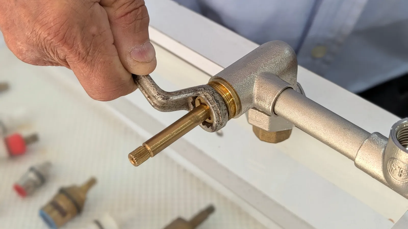 Mano sacando un vástago de latón de una grifería con una llave, junto a vástagos de repuesto en la vitrina