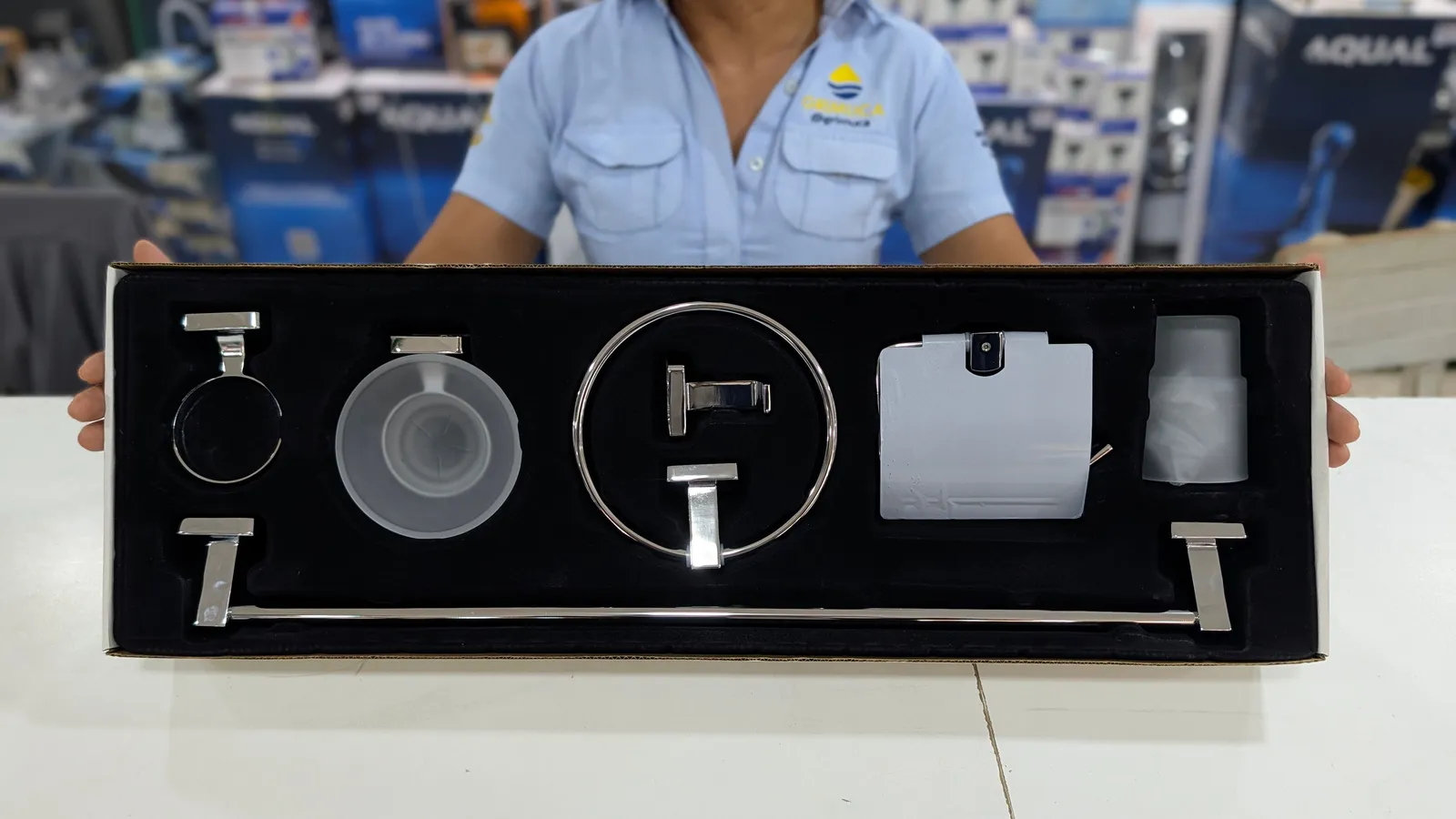 Vendedora de Grimuca mostrando un juego de accesorios de baño con jabonera en su caja, sobre el mostrador de la tienda
