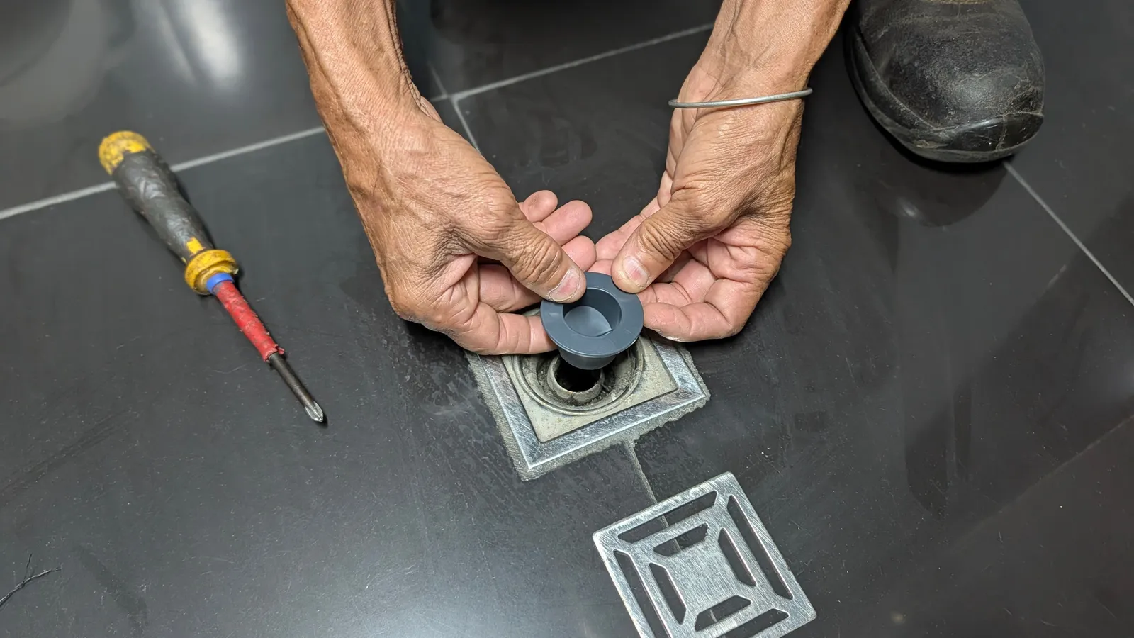 Manos colocando una válvula antiolor en el desagüe de una rejilla de piso, con un destornillador al lado