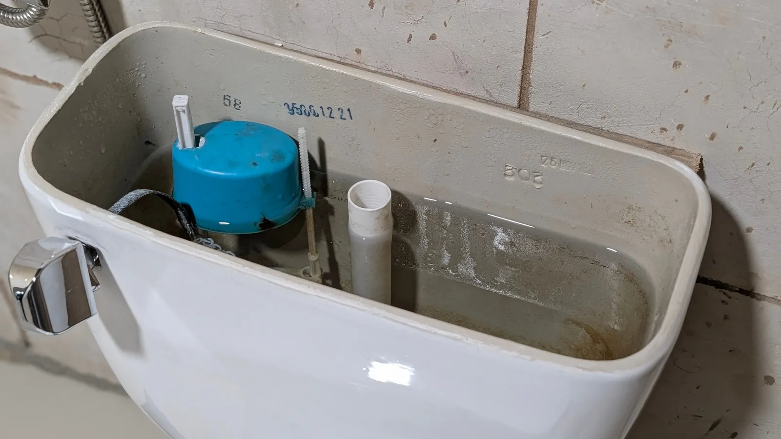 Tanque de inodoro abierto que muestra el herraje, la válvula de llenado azul y el tubo de rebose